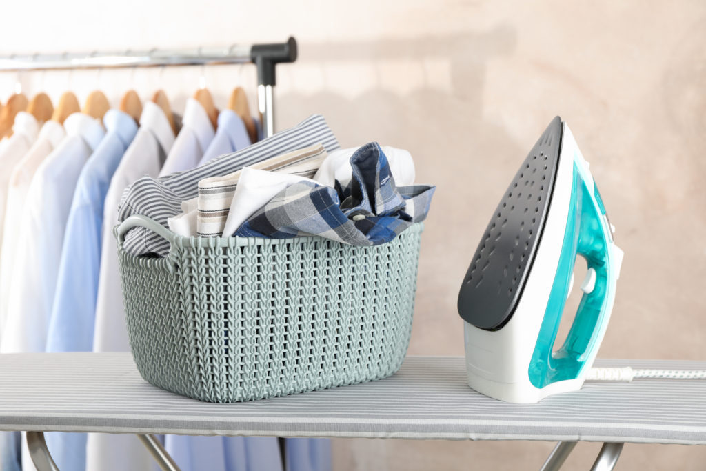 Basket with clean laundry and iron on ironing board, space for t